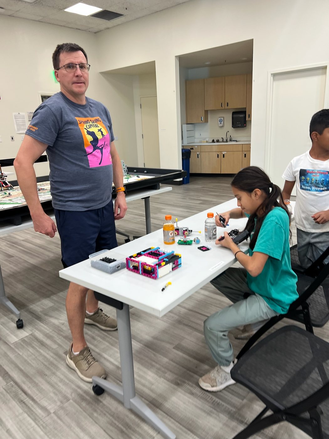 A Reno Rovers coach helping a student test a LEGO robotics build at a practice table